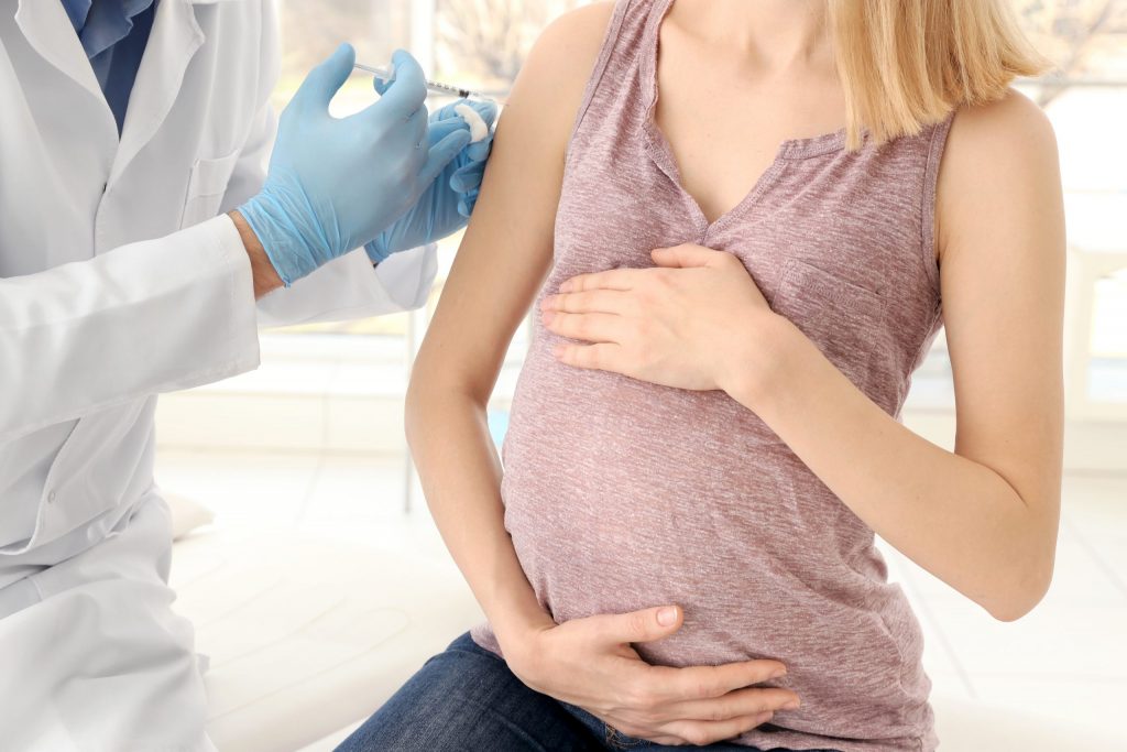 Vaccination concept. Male doctor vaccinating young pregnant woman
